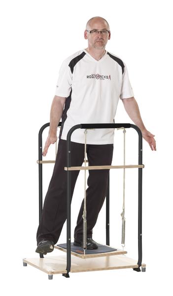 Mann trainiert Gleichgewicht auf Wackelbrett mit Haltegriff in Sportkleidung vor weißem Hintergrund.