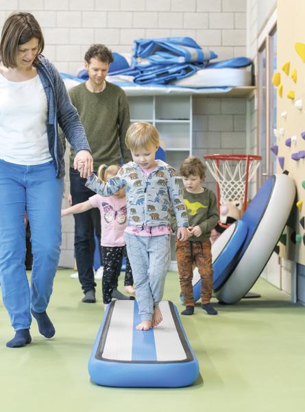 Kinder balancieren auf AirTrack Factory AirBeam im Sportunterricht mit Betreuung.