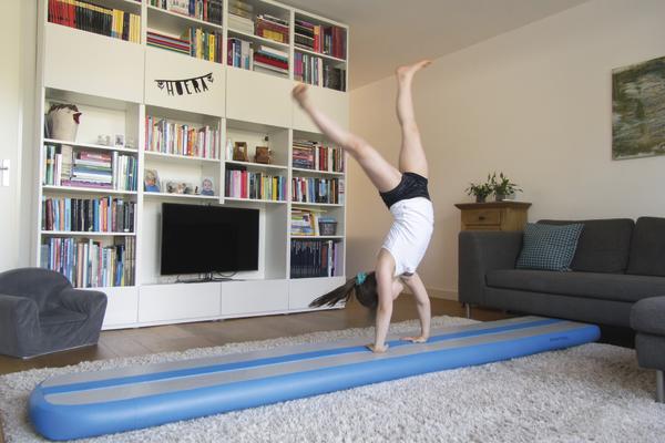 Kind trainiert Handstand auf AirTrack Factory AirBeam Blau im Wohnzimmer.