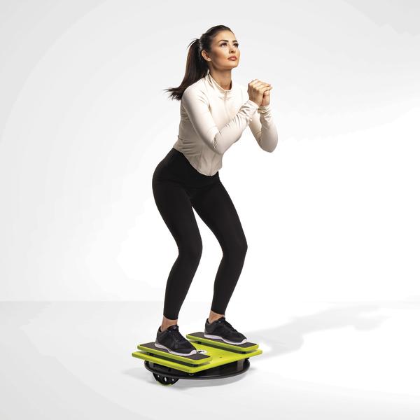 Frau trainiert Balance und Koordination auf einem grünen Balance-Board in Sportkleidung.