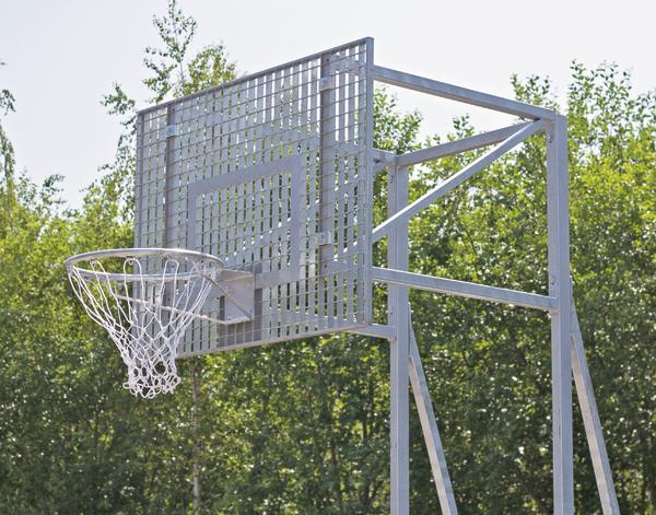 Outdoor-Basketballkorb mit Metallnetz vor grünem Wald an sonnigem Tag.