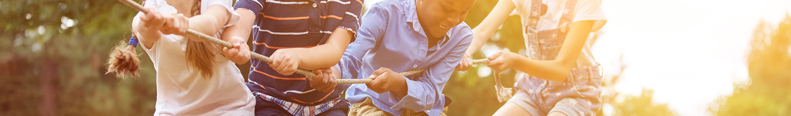Kinder ziehen im Freien an einem Seil, während die Sonne im Hintergrund scheint.