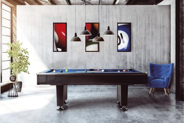 Billardtisch in modernem Raum mit Betonwand, drei Bildern und blauem Sessel neben Pflanze.