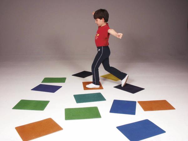 Kind springt auf bunten rechteckigen Matten auf weißem Boden vor grauem Hintergrund.