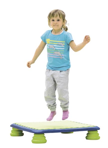 Kind springt auf einem bunten Trampolin, trägt blaues T-Shirt und graue Hose, weißer Hintergrund.