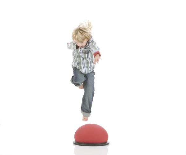 Kind springt barfuß auf großen roten Balance-Trainingsball vor weißem Hintergrund.