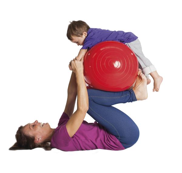 Frau macht Gymnastik mit Kind auf rotem Gymnastikball, spielerische Fitnessübung.