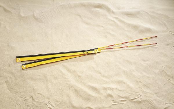 Gelbe Beachvolleyball-Netzantennen mit langen Griffen liegen auf hellem Sandstrand.