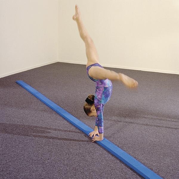 Junges Mädchen macht Handstand auf blauer Turnmatte in Trainingsraum.