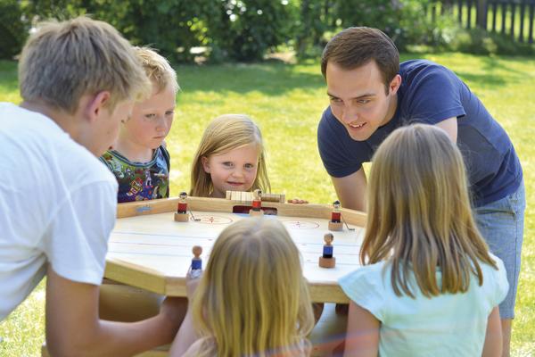 Kinder und Erwachsener spielen gemeinsam Tischhockey im Garten an sonnigem Tag.