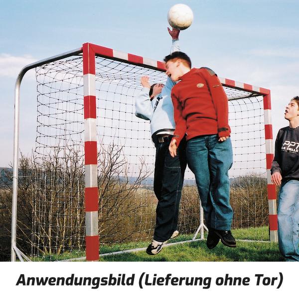 Junge Spieler springen und kämpfen um den Ball vor einem Handballtor im Freien.