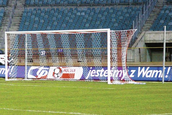 Fußballtor mit Netz auf grünem Spielfeld vor leeren Stadiontribünen und Werbebanner.