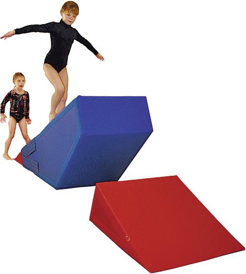 Kind balanciert auf blauem Schaumstoffblock, anderes Kind wartet, rote Rampe davor, Turnanzüge.