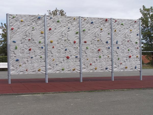 Kletterwand mit bunten Griffen auf rotem Fallschutzboden im Außenbereich.