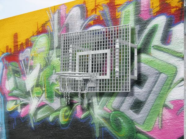 Basketballkorb mit Metallnetz vor bunter Graffiti-Wand auf gelbem Hintergrund.
