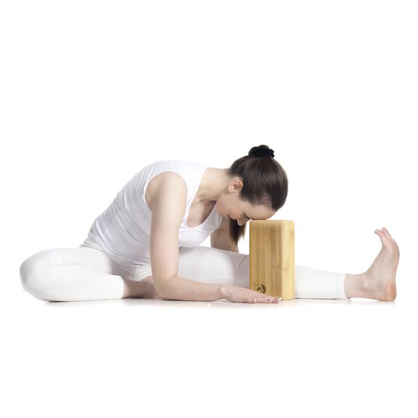 Frau in weißer Sportkleidung macht Yoga-Dehnübung mit Holzblock auf weißem Hintergrund.