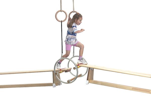 Mädchen balanciert auf Holzturngerät mit Ringen und Balancierbalken im Turnraum.