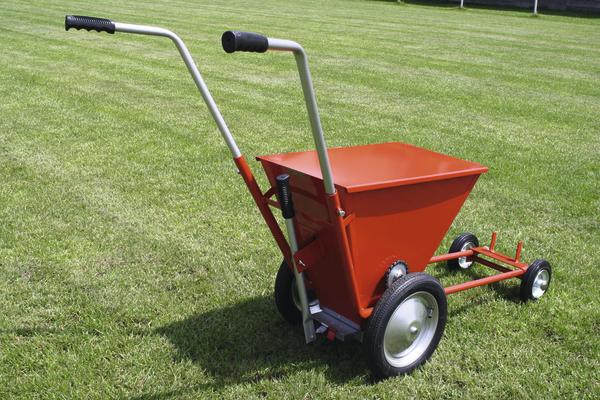 Roter Streuwagen auf grünem Rasen für gleichmäßige Düngung und Saatgutverteilung.