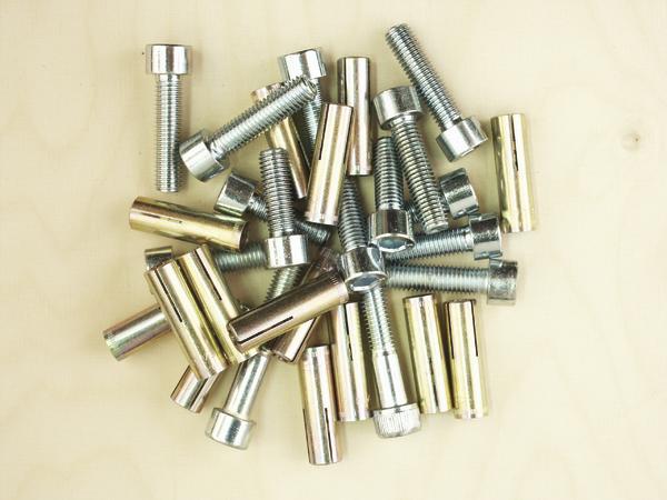 Verschiedene Metallbolzen und Schrauben auf hellem Holzuntergrund, Nahaufnahme.