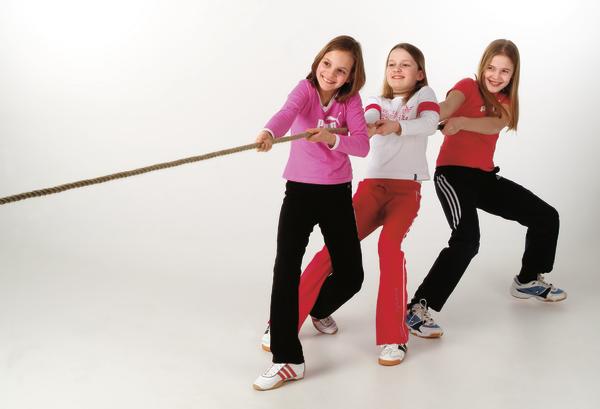 Drei Mädchen spielen Tauziehen, ziehen gemeinsam an einem Seil vor weißem Hintergrund.