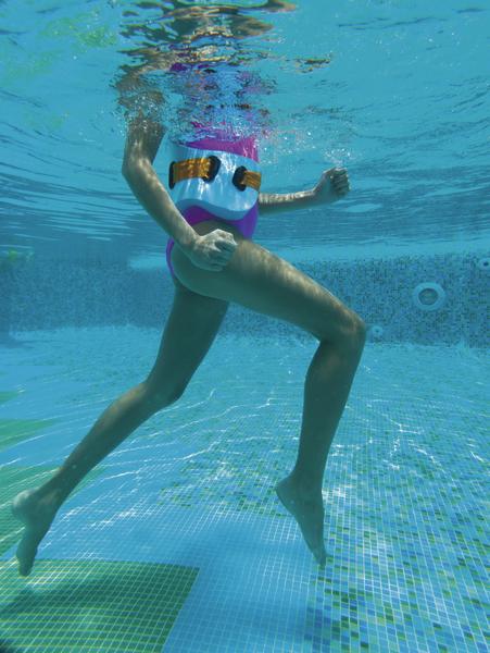 Kind mit Schwimmweste läuft unter Wasser im Schwimmbecken mit blauen Fliesen.