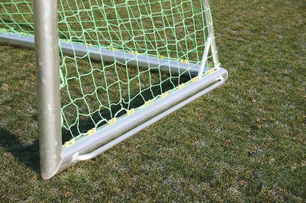 Fußballtor mit grünem Netz auf Rasenplatz bei Sonnenschein.