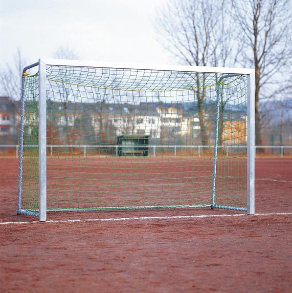 Fußballtor mit grünem Netz auf rotem Sportplatz bei bewölktem Himmel.
