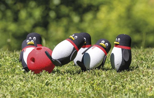Kleine Pinguin-Kegel beim Outdoor-Bowling auf grünem Rasen mit rotem Bowlingball.