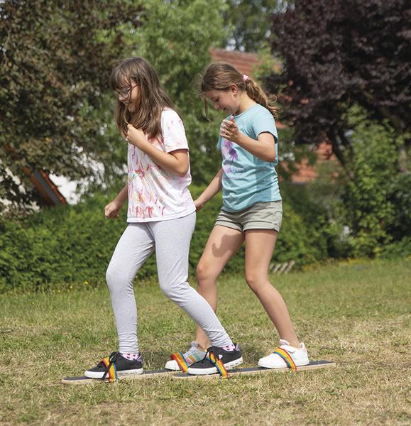 Zwei Mädchen spielen gemeinsam auf einem Holzbrett mit bunten Bändern im Garten.