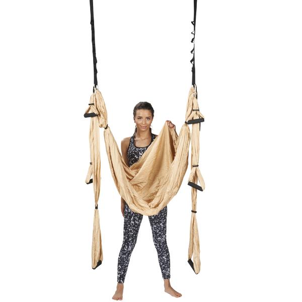 Frau steht in Yogahängematte aus Seide, bereit für Aerial Yoga-Übung, weißer Hintergrund.