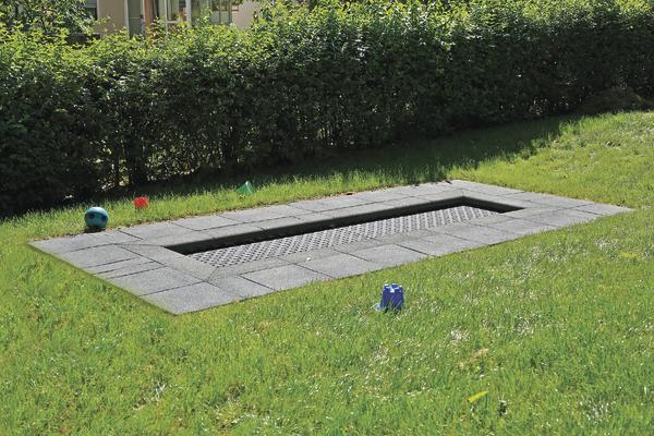 Eingebautes Bodentrampolin im Garten mit grünem Rasen und Hecke im Hintergrund.