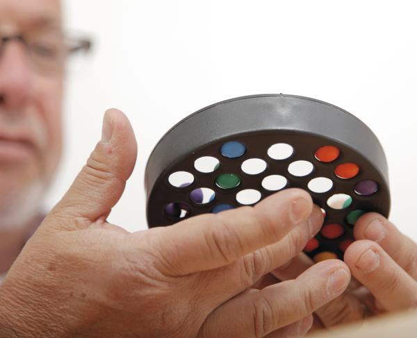 Älterer Mann hält ein rundes Farbsehtestgerät mit bunten Farbfiltern in der Hand.