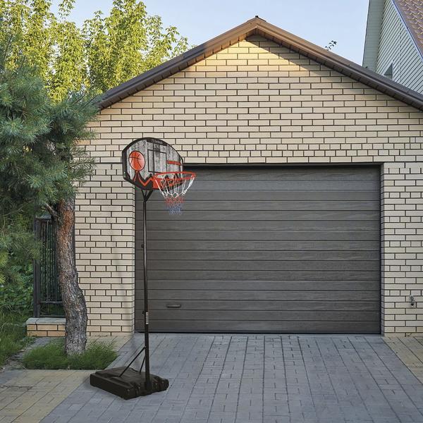 Mobiler Basketballkorb mit Ball vor moderner Garage und grünem Baum im Garten.