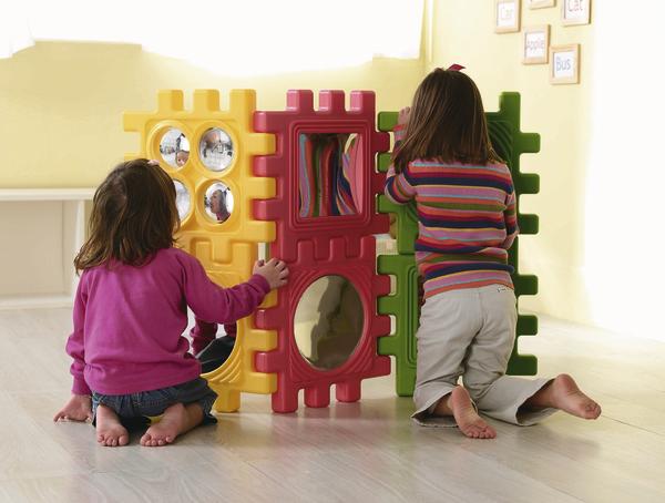 Kinder spielen mit bunten, großen Steckbausteinen auf hellem Boden im Kinderzimmer.