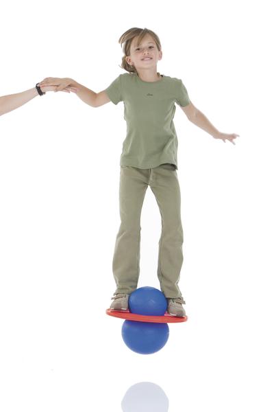 Kind balanciert auf blauem Ball und roter Platte, hält Hand zur Stabilisierung.