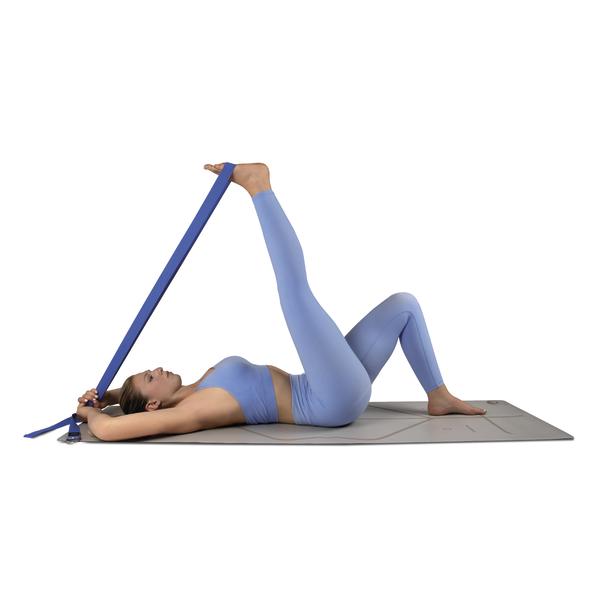Frau macht Bein-Dehnübung mit Yoga-Gurt auf Matte, trägt blaues Sportoutfit.