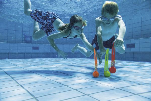 Kinder tauchen im Schwimmbecken und spielen mit bunten Tauchspielzeugen unter Wasser.