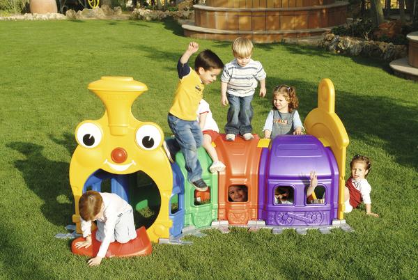 Kinder spielen auf einem bunten Spielzeug-Zug im Garten auf grünem Rasen.