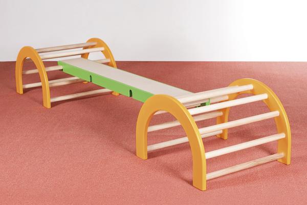 Balancierbalken mit orangem Holzrahmen und grünem Mittelteil auf rotem Boden.