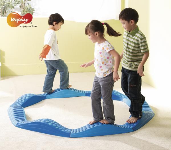 Kinder balancieren barfuß auf einem blauen Balancierkreis im Innenraum, spielerisch lernen.