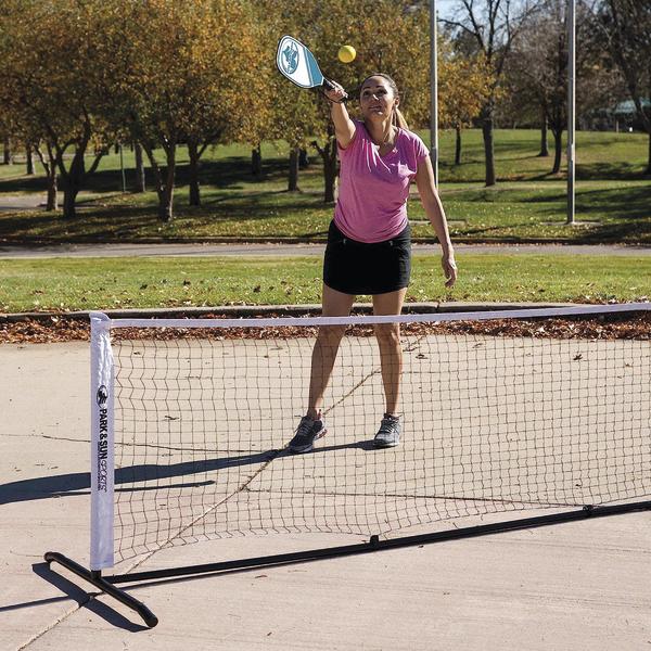 Frau spielt Pickleball im Freien auf Asphaltplatz mit Netz und gelbem Ball im Herbst.