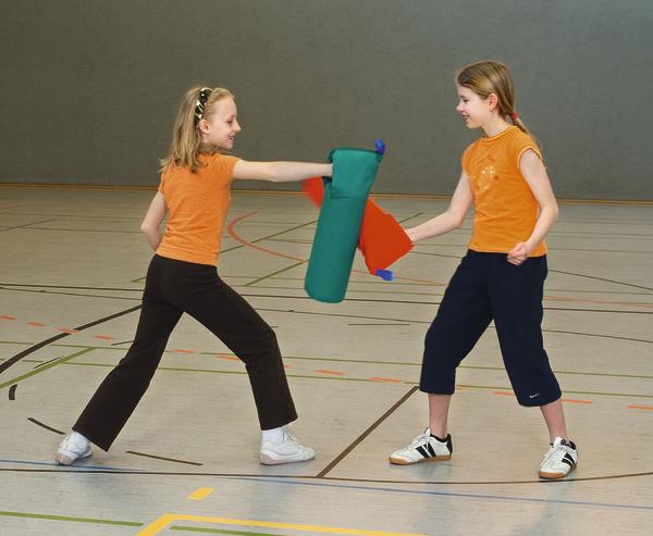 Zwei Mädchen in Sportkleidung spielen mit Schaumstoffschwertern in der Turnhalle.