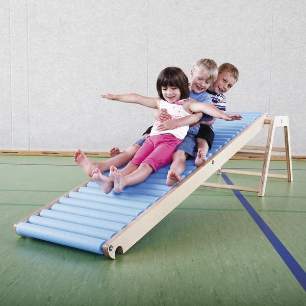 Drei Kinder rutschen gemeinsam auf einer blauen Rollrutsche in einer Turnhalle.