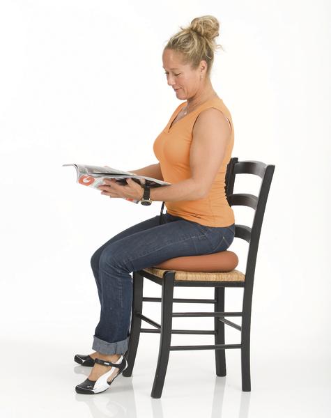 Frau sitzt auf Stuhl mit Sitzkissen und liest entspannt eine Zeitschrift.