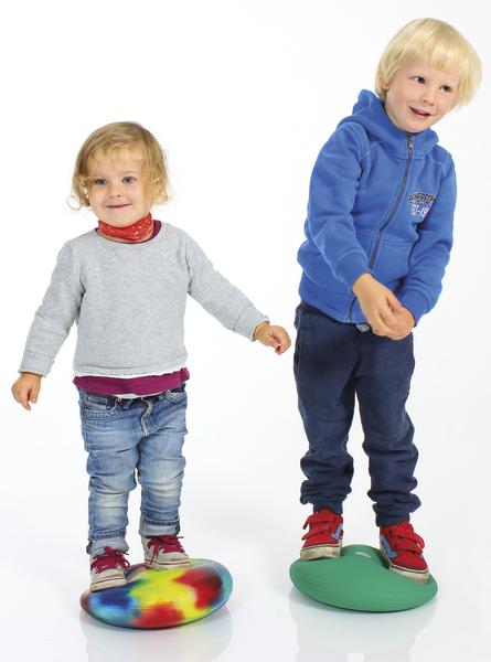 Zwei Kinder balancieren auf bunten Balancekissen vor weißem Hintergrund.