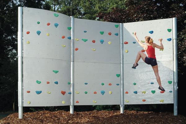 Frau klettert an bunter Outdoor-Kletterwand im Park bei Sonnenschein.