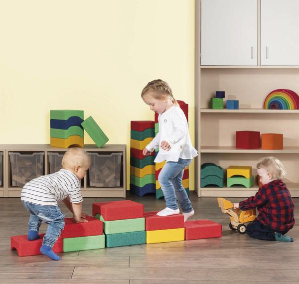 Drei kleine Kinder spielen in einem Raum mit bunten Schaumstoffbausteinen.