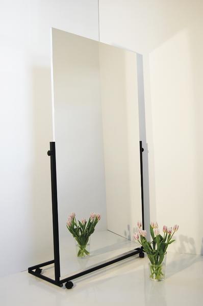 Großer Standspiegel mit schwarzem Rahmen und Vase mit rosa Tulpen auf weißem Boden.