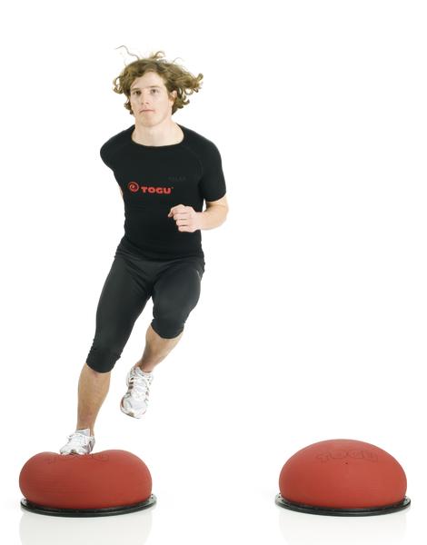 Mann trainiert Balance und Koordination auf roten Togu Balance Pads in Sportkleidung.