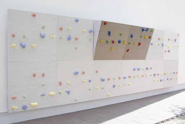 Kletterwand mit bunten Griffen an einer weißen Außenwand, ideal für Klettertraining.